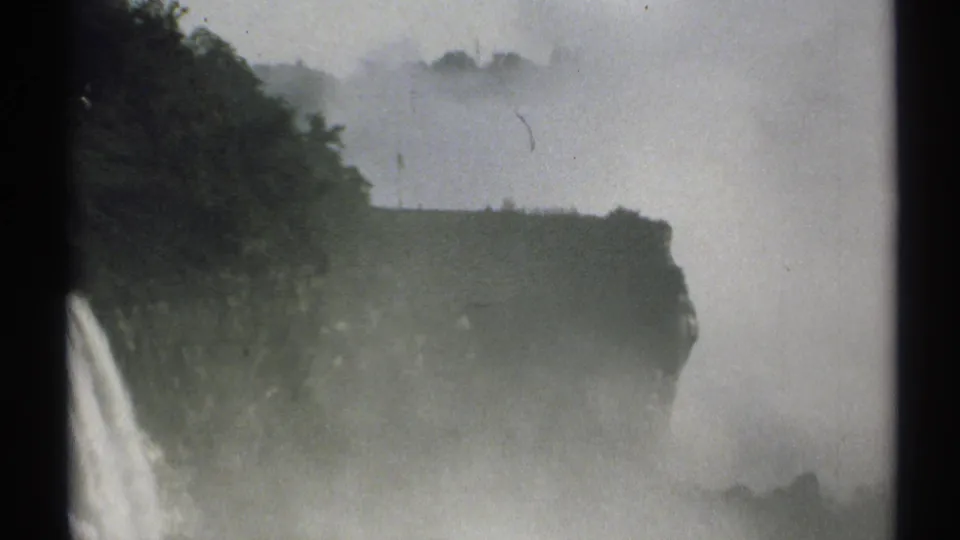 1971 New York 8mm frame showing a waterfall at the lower left, a dark cliff line, trees, and dense mist from the falling water.