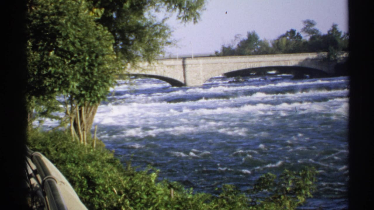 Rapids below a stone bridge, framed by trees and dark film borders.