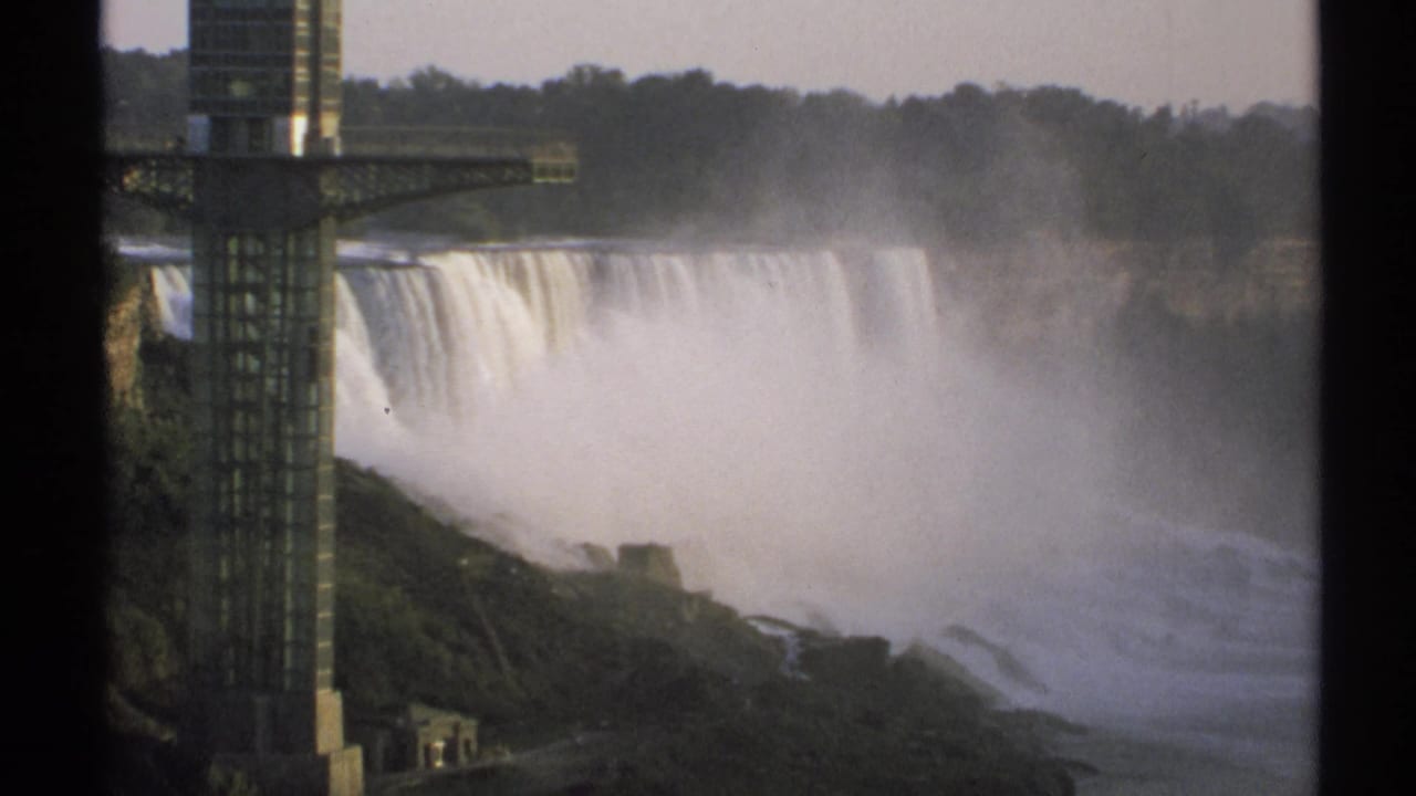Waterfall and mist beside a tall observation tower, with trees along the far rim.