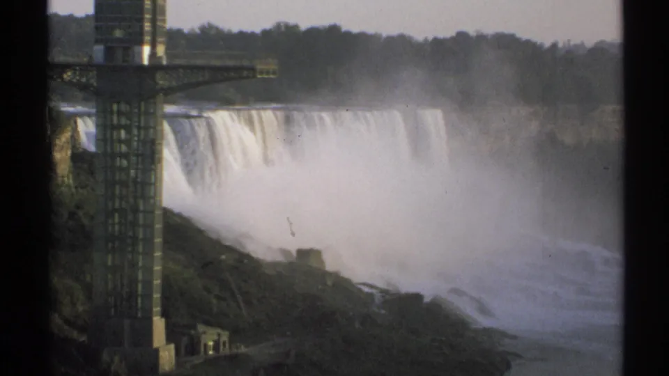 1971 8mm New York travel frame with Niagara Falls, dense mist, rocky slopes, water below, and the observation tower at left.