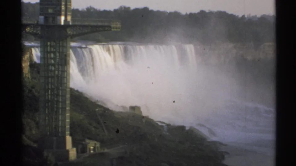 1971 8mm frame of Niagara Falls in New York, showing broad falling water, mist, a foreground observation tower, and visible film borders.