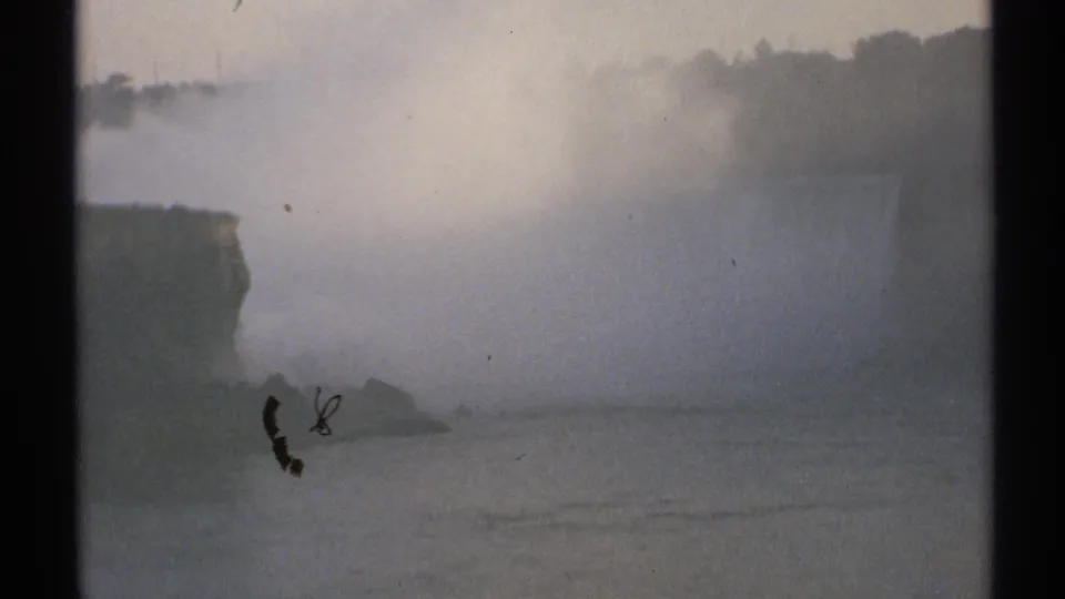1971 New York 8mm frame showing heavy mist over broad water with a dark cliff edge and distant tree line.