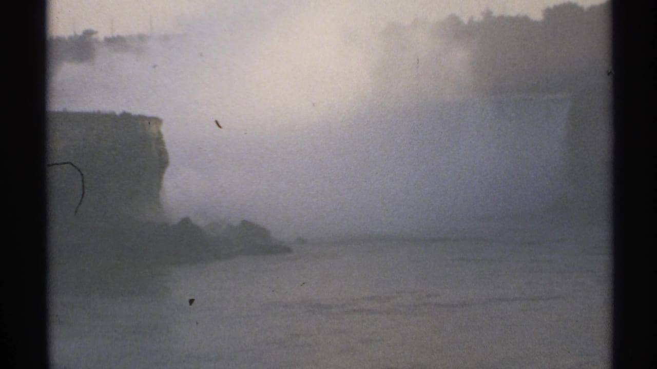Foggy river view with cliff face, water spray, and distant shoreline.