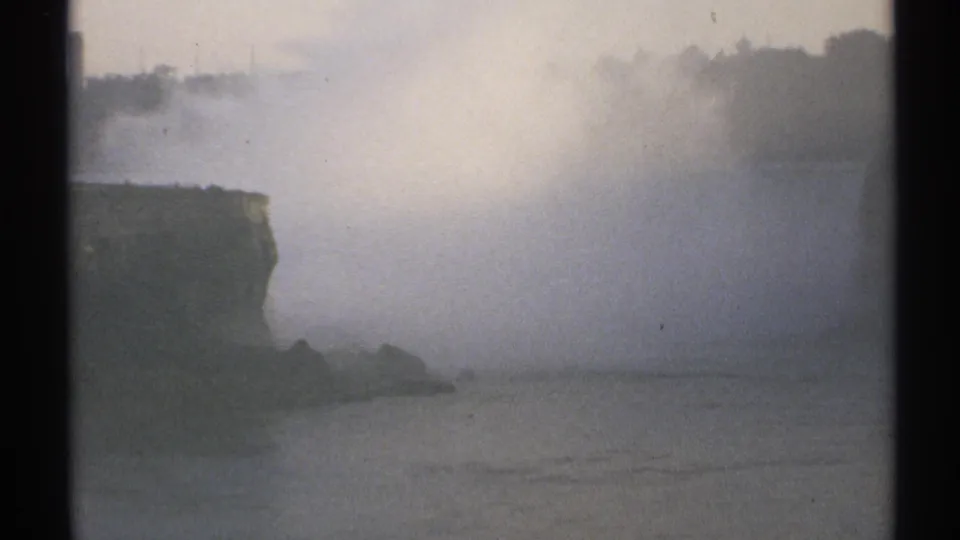 1971 New York 8mm frame with soft-focus mist rising over water near a dark cliff and low rocky shore.