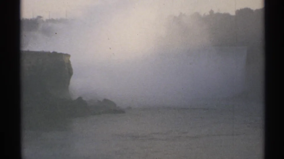 1971 8mm view of Niagara Falls partly obscured by mist, with cliff edges, river water, and visible film-frame borders.