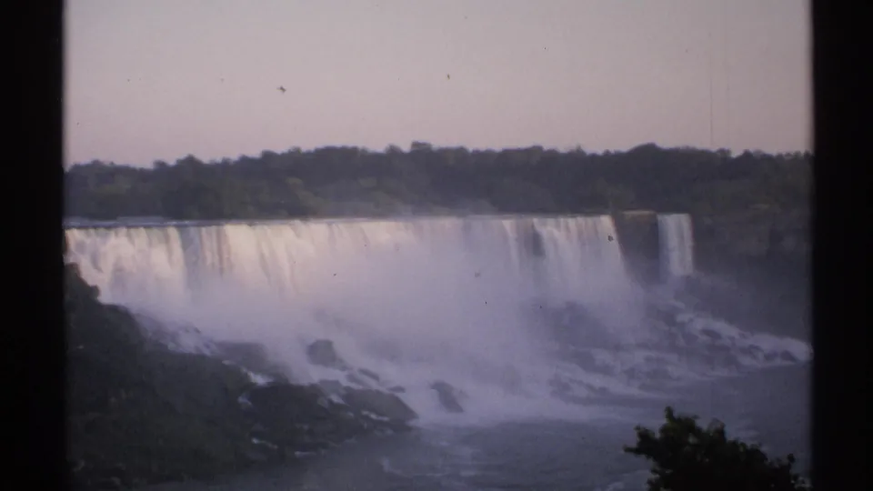 1971 New York home-movie frame showing Niagara Falls, broad falling water, mist clouds, dark trees, and 8mm frame edges.