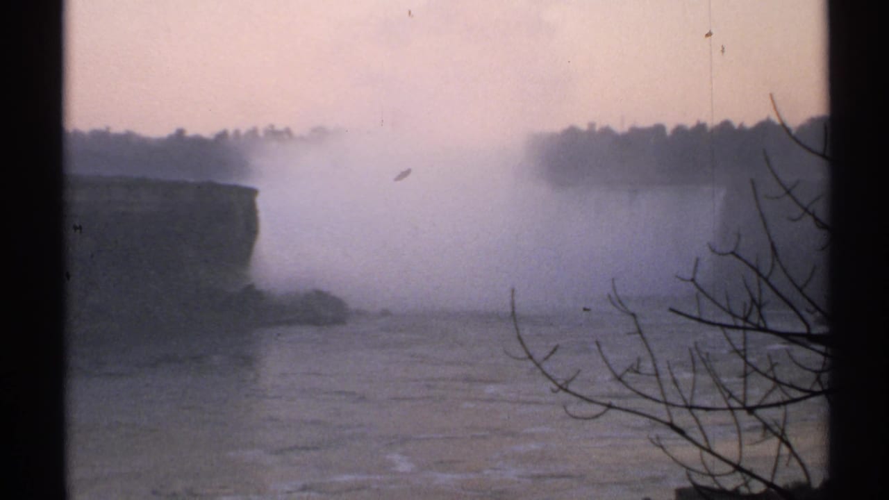 Mist over Niagara Falls with river water below and bare branches at right.