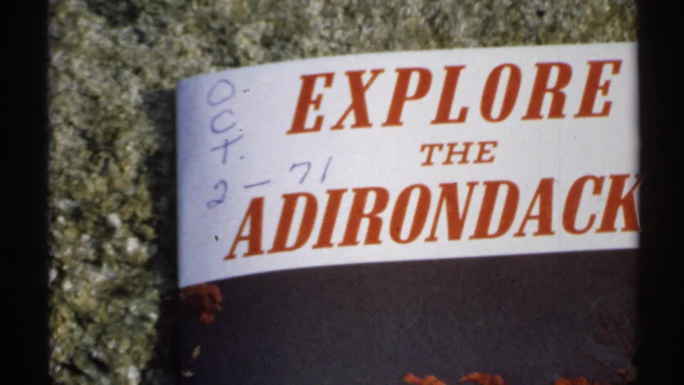Close 8mm frame of a public sign reading Explore the Adirondack, with handwritten Oct. 2, 71 marks visible on the sign face.