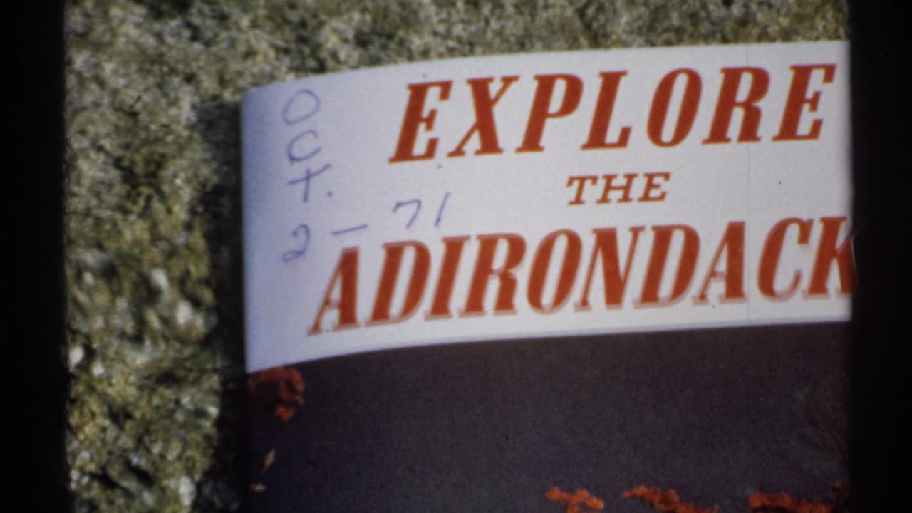 Close view of an Explore the Adirondacks brochure with handwritten date marks on a stone surface.