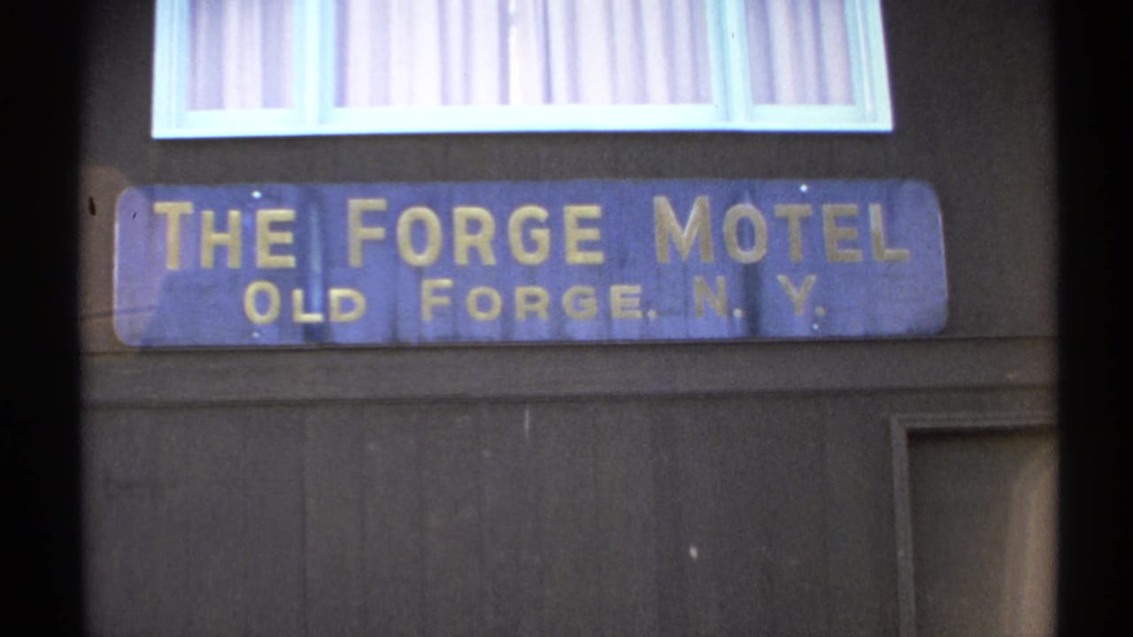 Blue sign reading The Forge Motel, Old Forge, N.Y., mounted below a window.