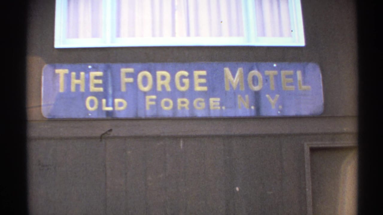 Blue sign reading The Forge Motel, Old Forge, N.Y., on a wooden building exterior.