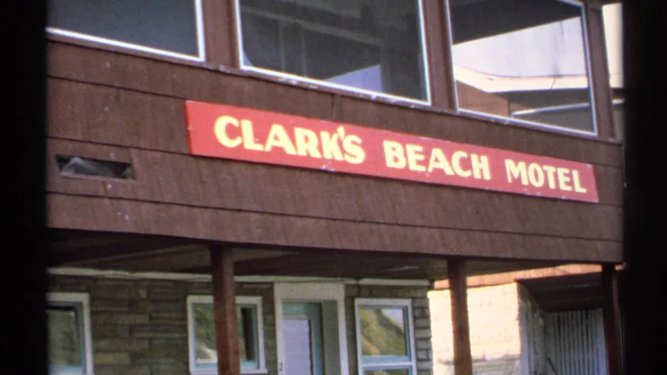 Close 1971 home-movie view of the Clark's Beach Motel sign, with brown siding, windows, and lower doorway details visible below.