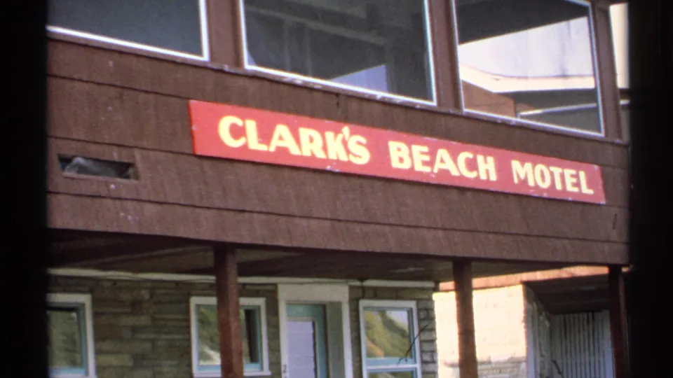 1971 New York 8mm frame of Clark's Beach Motel signage framed by dark film edges, with wood siding, windows, posts, and doors below.