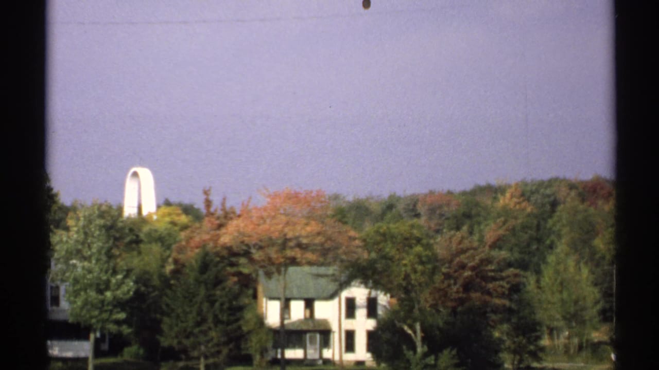 White house among autumn trees with a pale sky and dark vertical film border.
