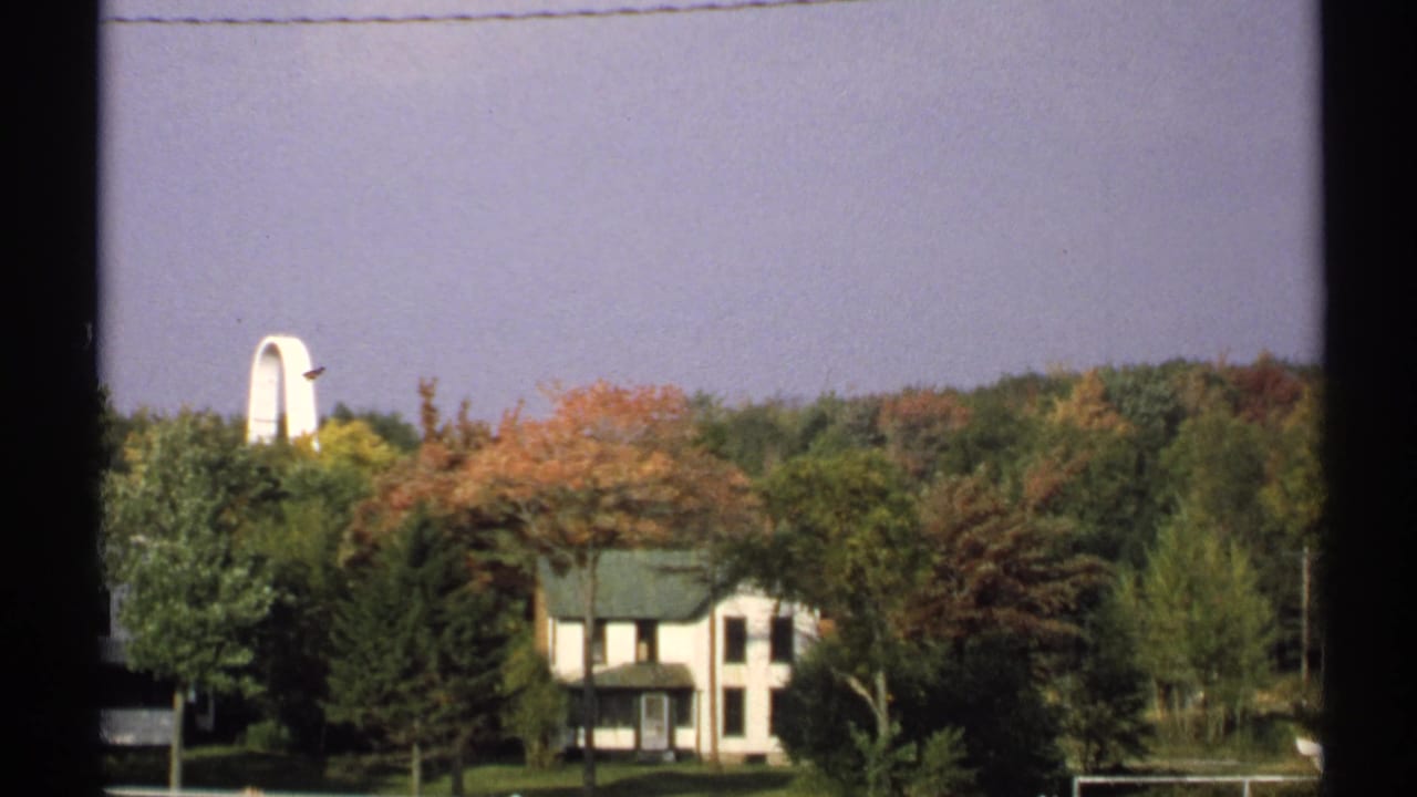 Autumn trees and a white house seen through dark vertical framing.