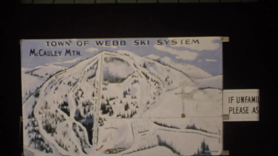 1971 New York 8mm frame showing a Town of Webb McCauley Mountain ski-system map sign and partial notice indoors or under shade.