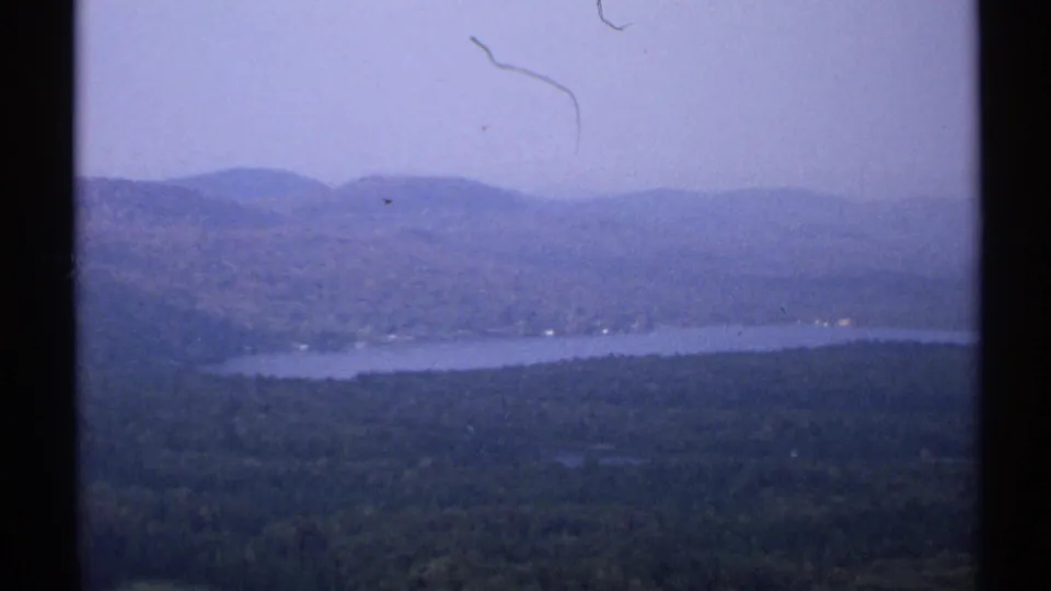 1971 New York home-movie vista of a lake among wooded hills, softened by haze and 8mm film grain.