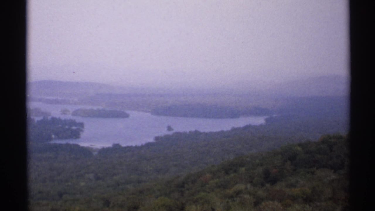 Hazy mountain overlook with a lake, forested hills, and dark film borders.