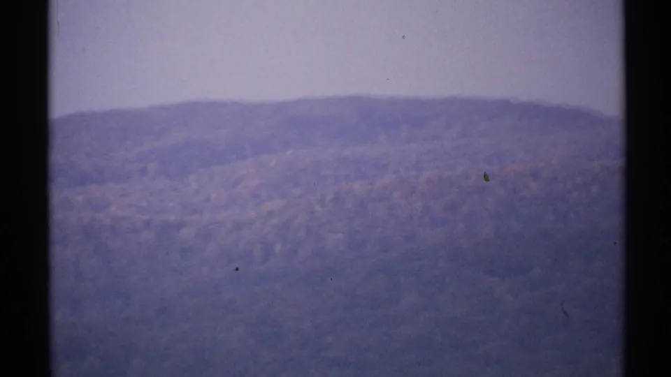 1971 New York 8mm frame showing a hazy wooded ridge in autumn tones, with no identifiable landmark visible.