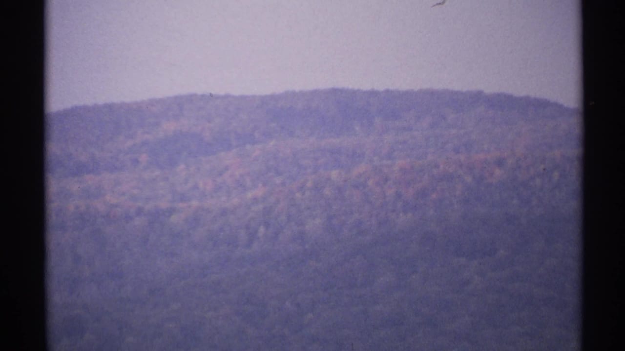 1971 New York 8mm frame showing a distant hazy mountain ridge with muted autumn colors and dark film borders.