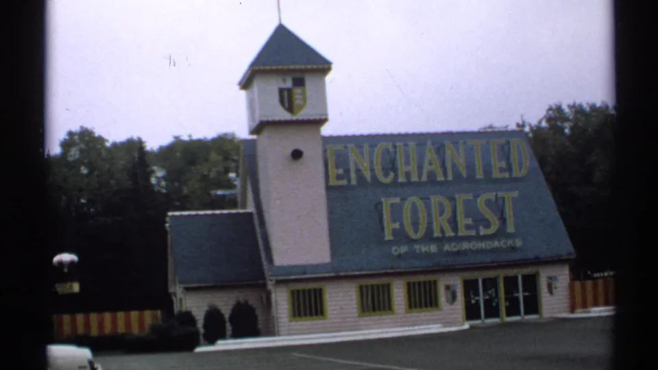 1971 New York frame of an Enchanted Forest of the Adirondacks exterior with tower, crest, empty pavement, and large sign.