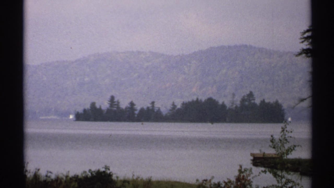 Similar lake view with island, hills, shoreline vegetation, and dark film edge.