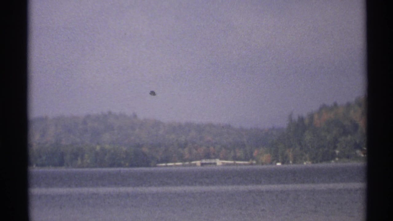 1971 New York 8mm frame holds on the lake and distant wooded shoreline with a small bridge-like structure visible.
