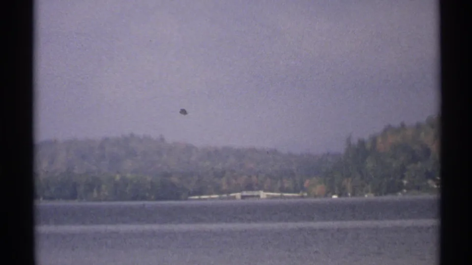 1971 New York 8mm frame holds on the lake and distant wooded shoreline with a small bridge-like structure visible.