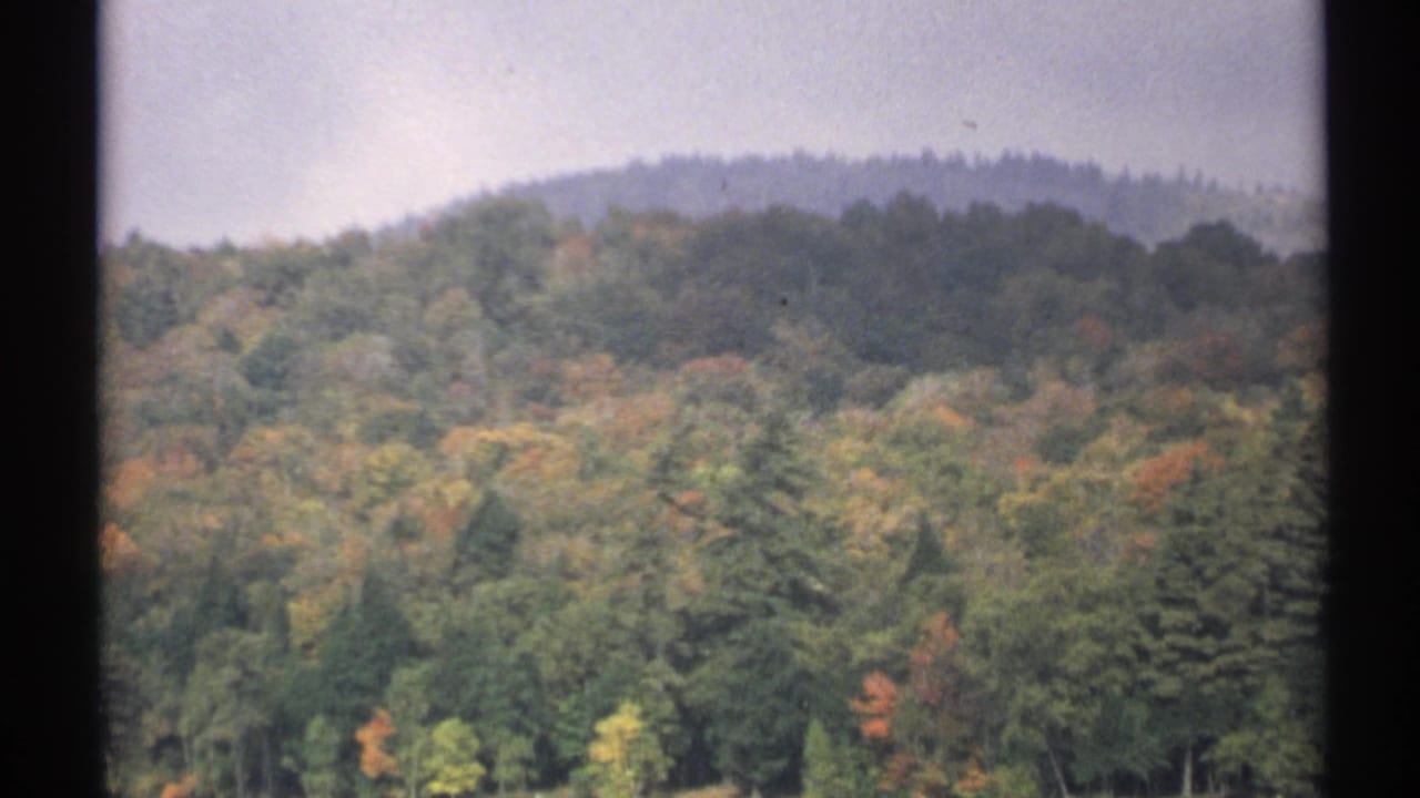 1971 New York 8mm frame showing a wooded hillside with early autumn color beyond still lake water.