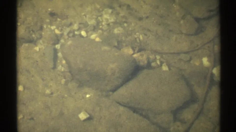 1971 New York 8mm frame looking into clear shallow lake water over smooth stones and pale pebbles.