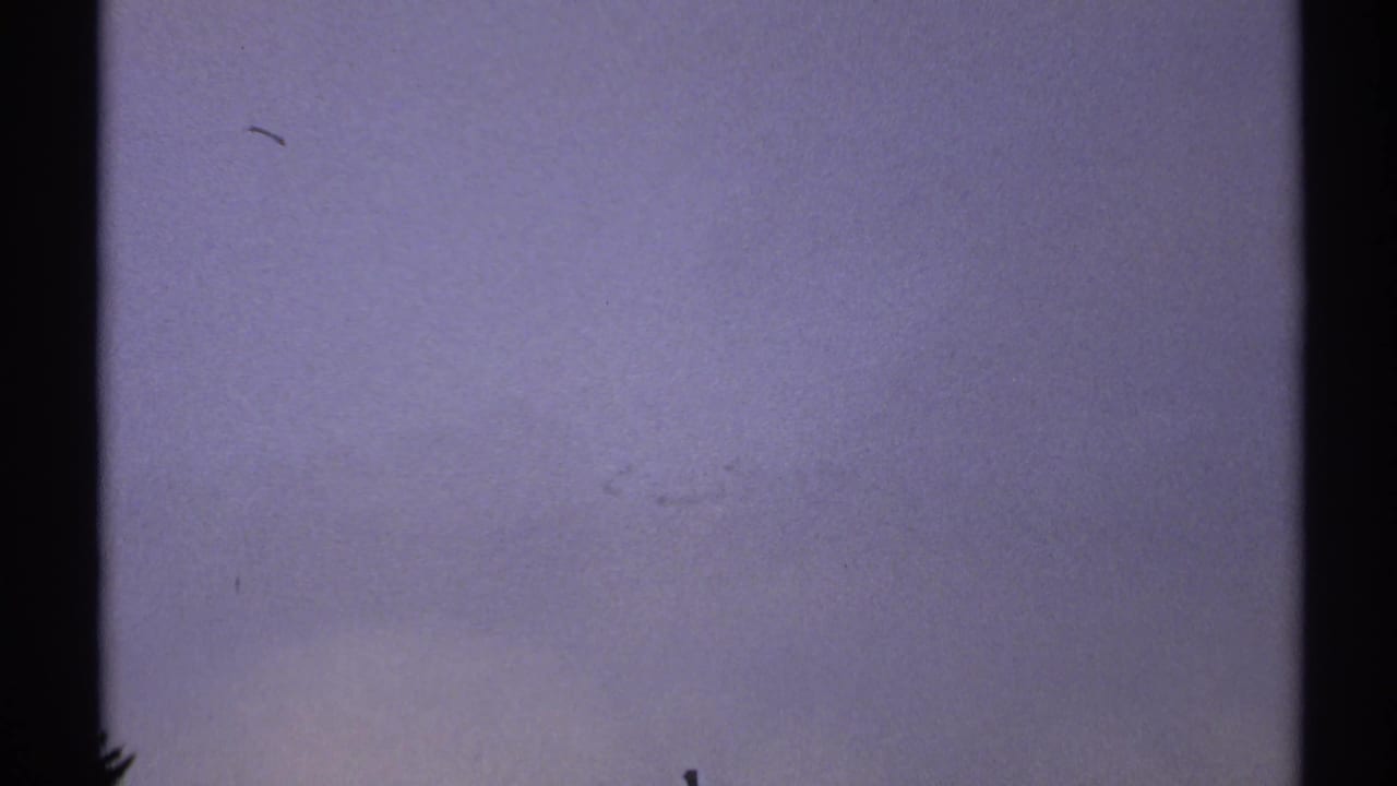 Soft, mostly featureless 8mm frame with blue-gray exposure, faint film marks, and black vertical edges.