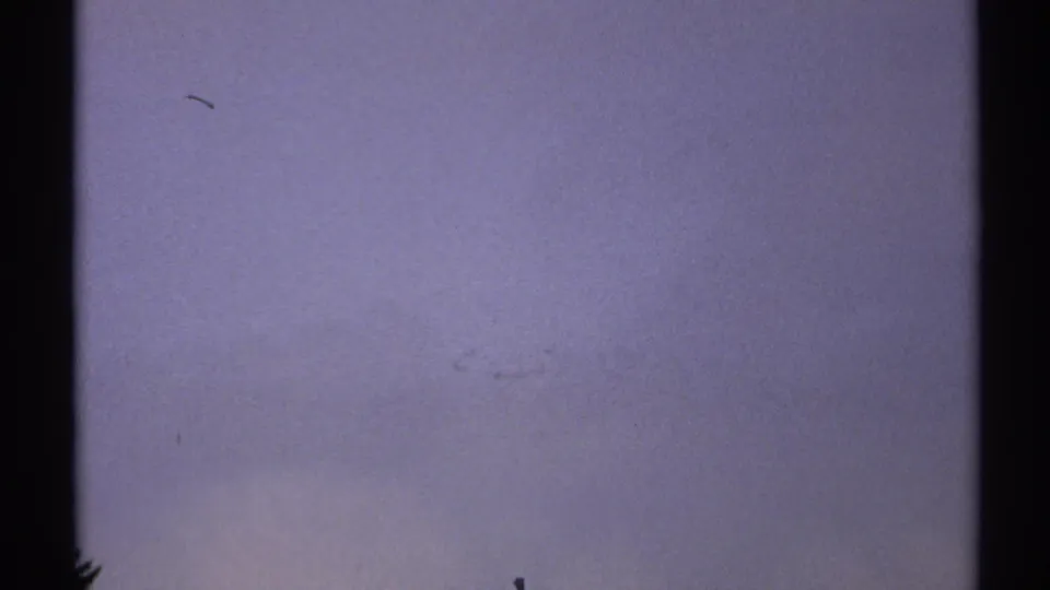 Soft, mostly featureless 8mm frame with blue-gray exposure, faint film marks, and black vertical edges.