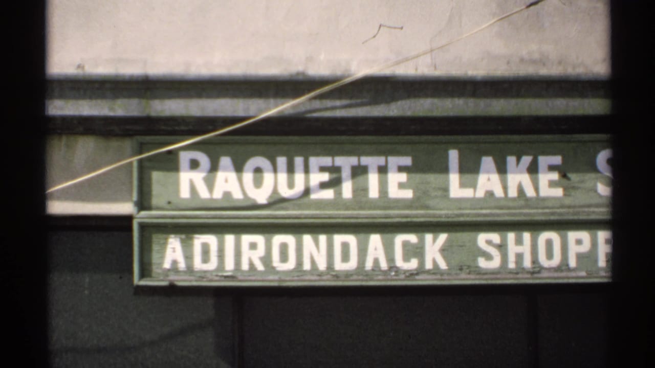 Close 8mm view of a green Raquette Lake Adirondack Shop sign on a building facade in New York.