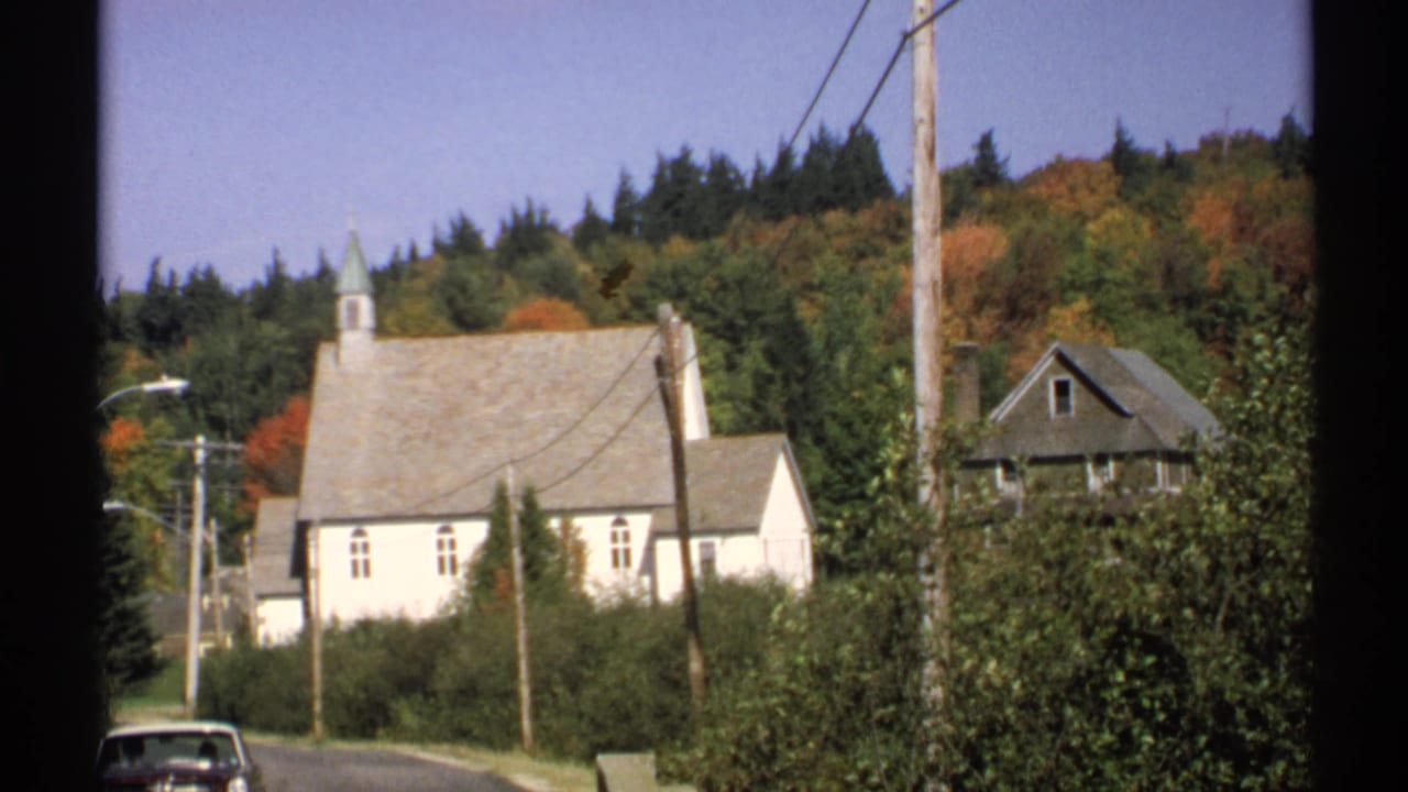 White church beside a roadside with utility poles, a house, trees, and a car at the lower edge.