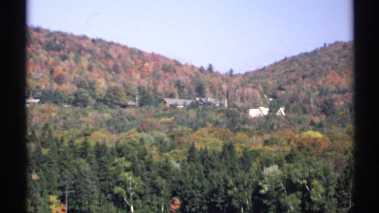 1971 New York 8mm frame of a wooded hillside with scattered houses among green and autumn-colored trees.