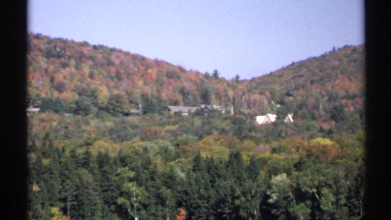 1971 New York 8mm frame showing fall-colored hills, evergreen trees, and small rural homes in the distance.