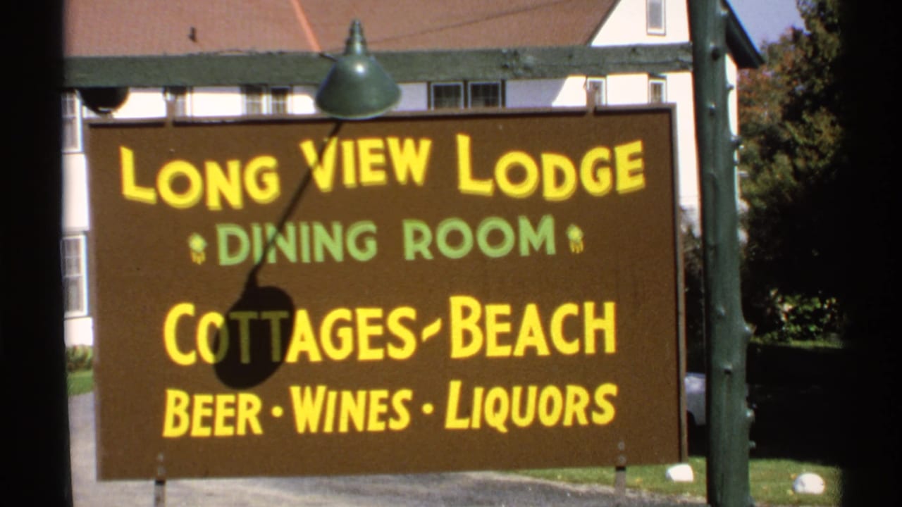 1971 New York home-movie frame showing the Long View Lodge sign beside a post, with a building and trees behind it.