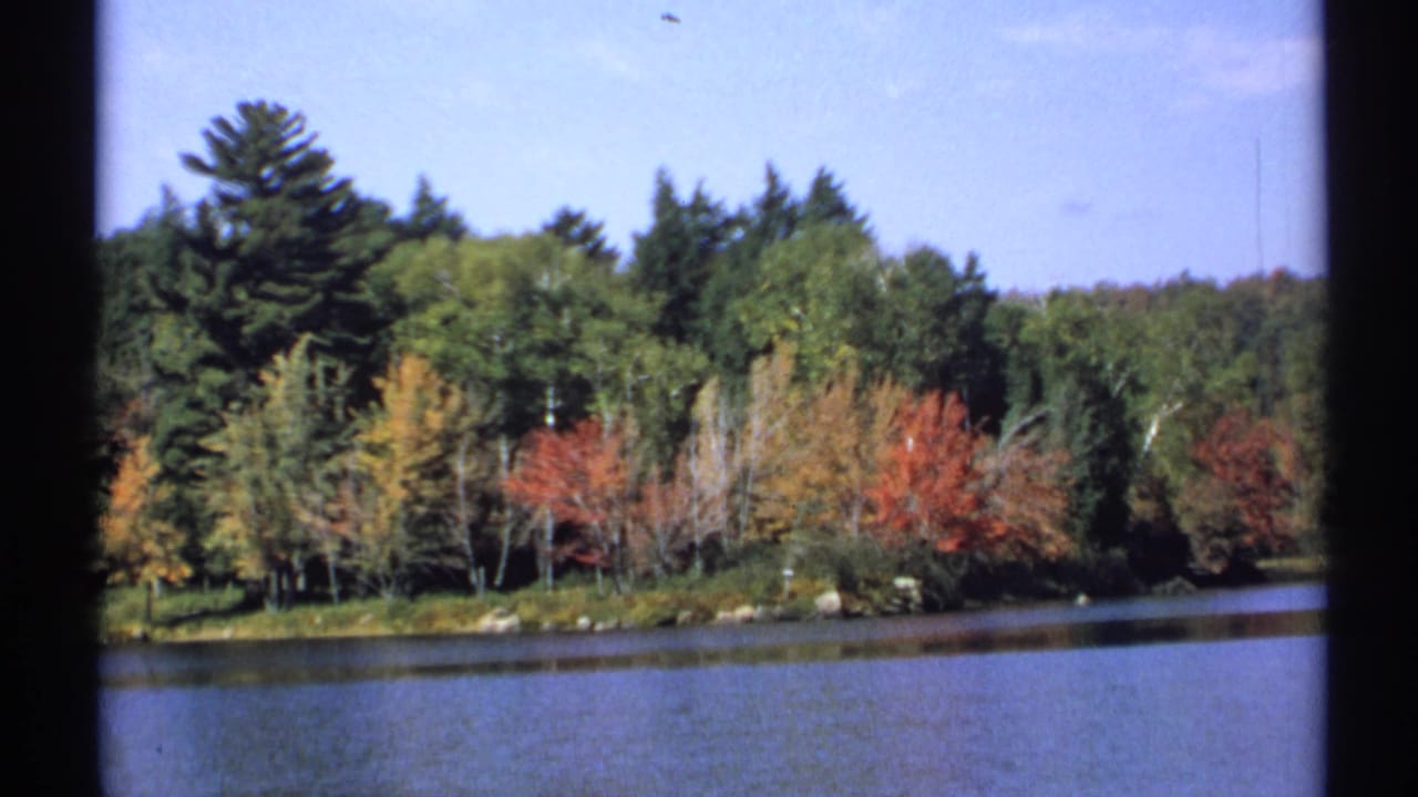 1971 New York 8mm frame of a lake foreground and tree-lined shore with bright fall colors.