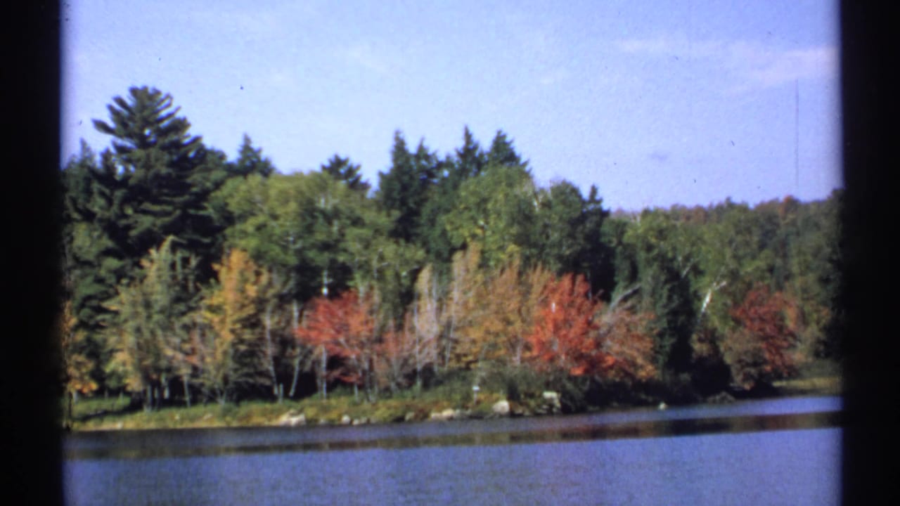 1971 New York 8mm frame holding on a calm lake and colorful wooded shoreline in autumn.