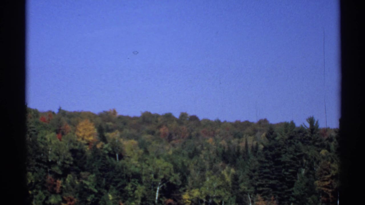 1971 New York 8mm still of a wooded autumn hillside, with window edges and visible film texture framing the view.
