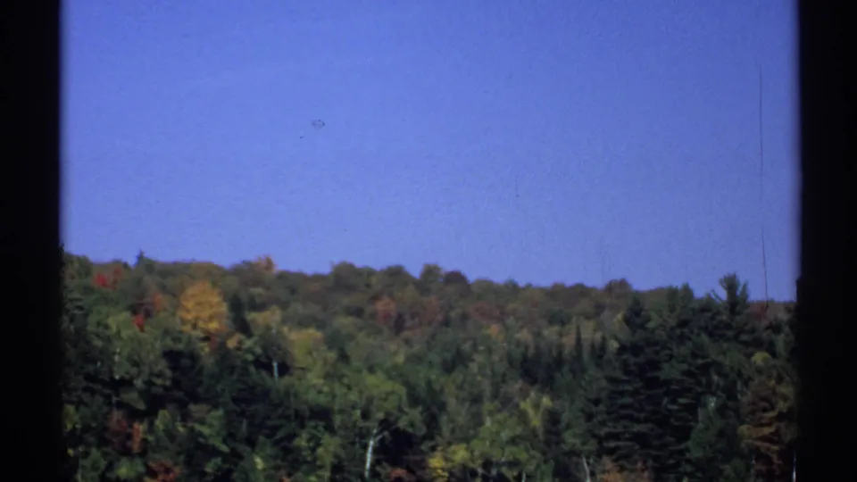 1971 New York 8mm still of a wooded autumn hillside, with window edges and visible film texture framing the view.