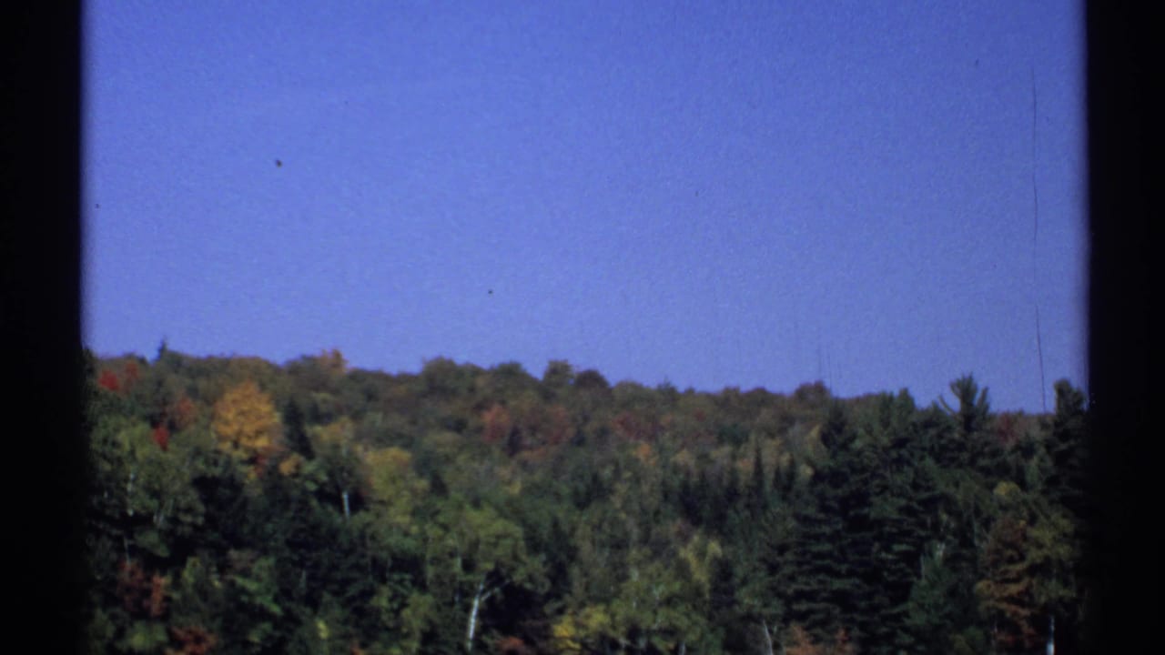 Distant wooded ridge under blue sky with autumn color and dark film borders.