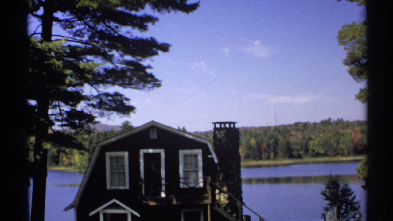 1971 New York 8mm frame of the cabin by the lake, framed by trees with autumn woods across the water.