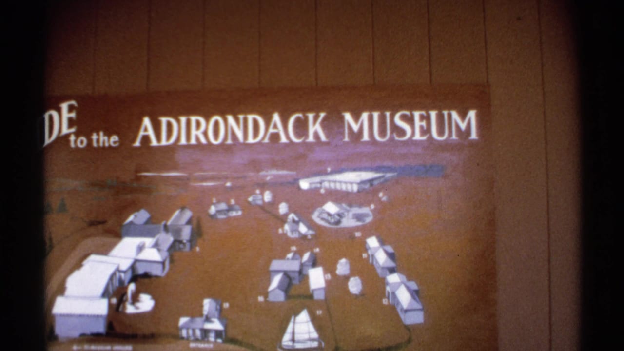 The Adirondack Museum guide board fills the frame, with illustrated buildings, paths, and a sailboat symbol visible on the map.