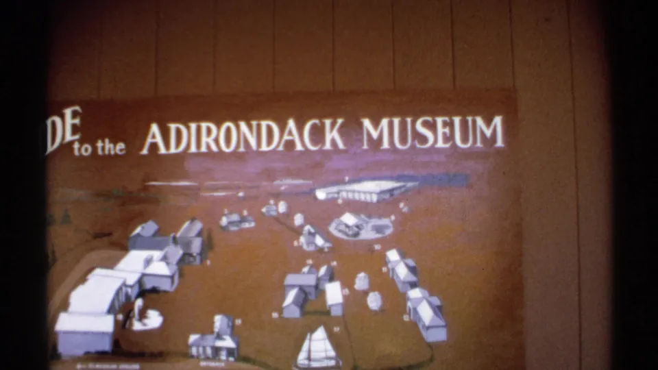 The Adirondack Museum guide board fills the frame, with illustrated buildings, paths, and a sailboat symbol visible on the map.