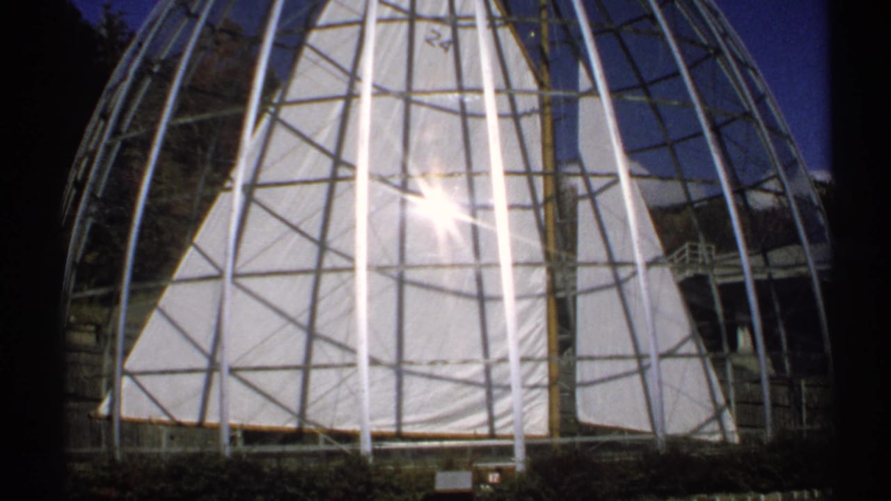 1971 New York home-movie frame showing a geodesic dome structure with metal ribs, translucent panels, and sun glare.