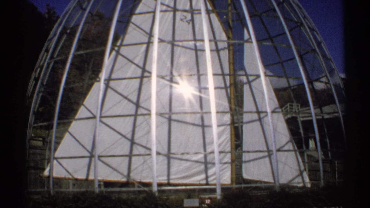 A close visitor-shot view of the dome's metal framework and pale panels, with strong sunlight blooming through the structure.