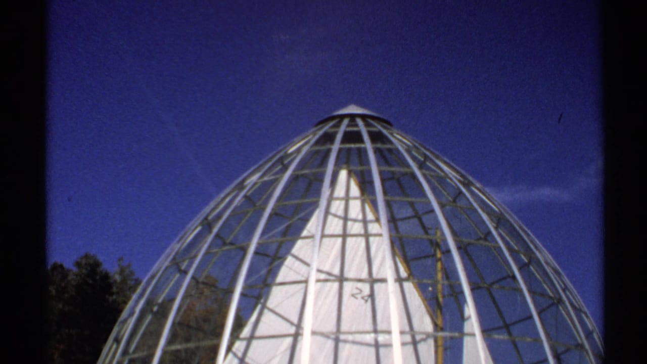 The camera tilts upward to show the dome's rounded top and metal lattice against a deep blue New York sky.