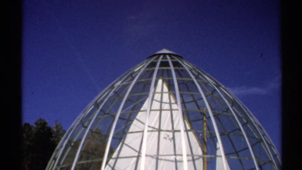 The camera tilts upward to show the dome's rounded top and metal lattice against a deep blue New York sky.