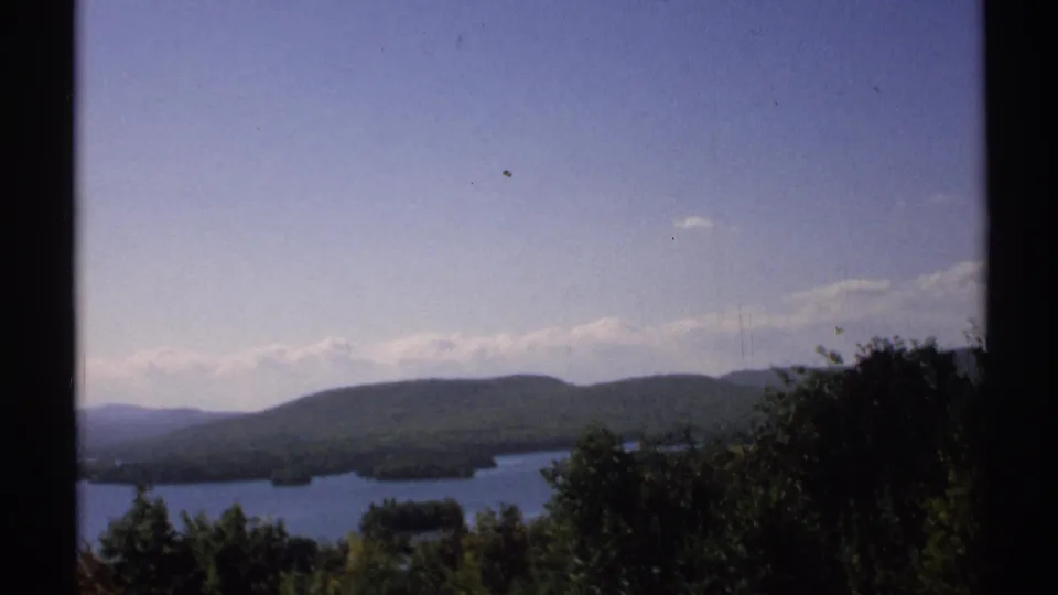 1971 New York scenic lake footage shows wooded hills, small islands, and a pale sky viewed past a dark vertical divider.